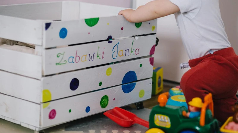 Dziecko wkłada zabawki do drewnianej skrzynki
