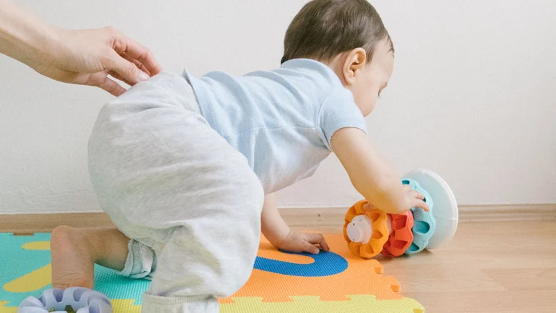 Małe dziecko raczkuje po kolorowej piankowej macie puzzlowej, sięgając po zabawkę