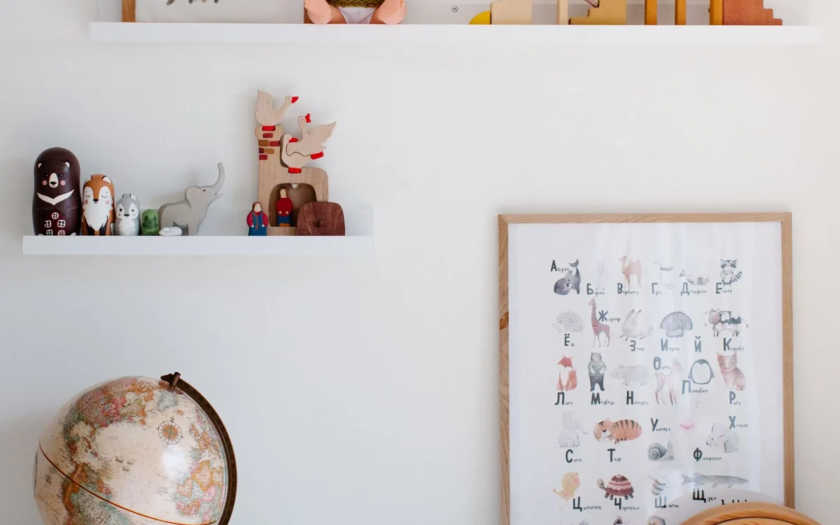 Otwarte półki ścienne z drewnianymi figurkami i plakat z alfabetem nad regałem