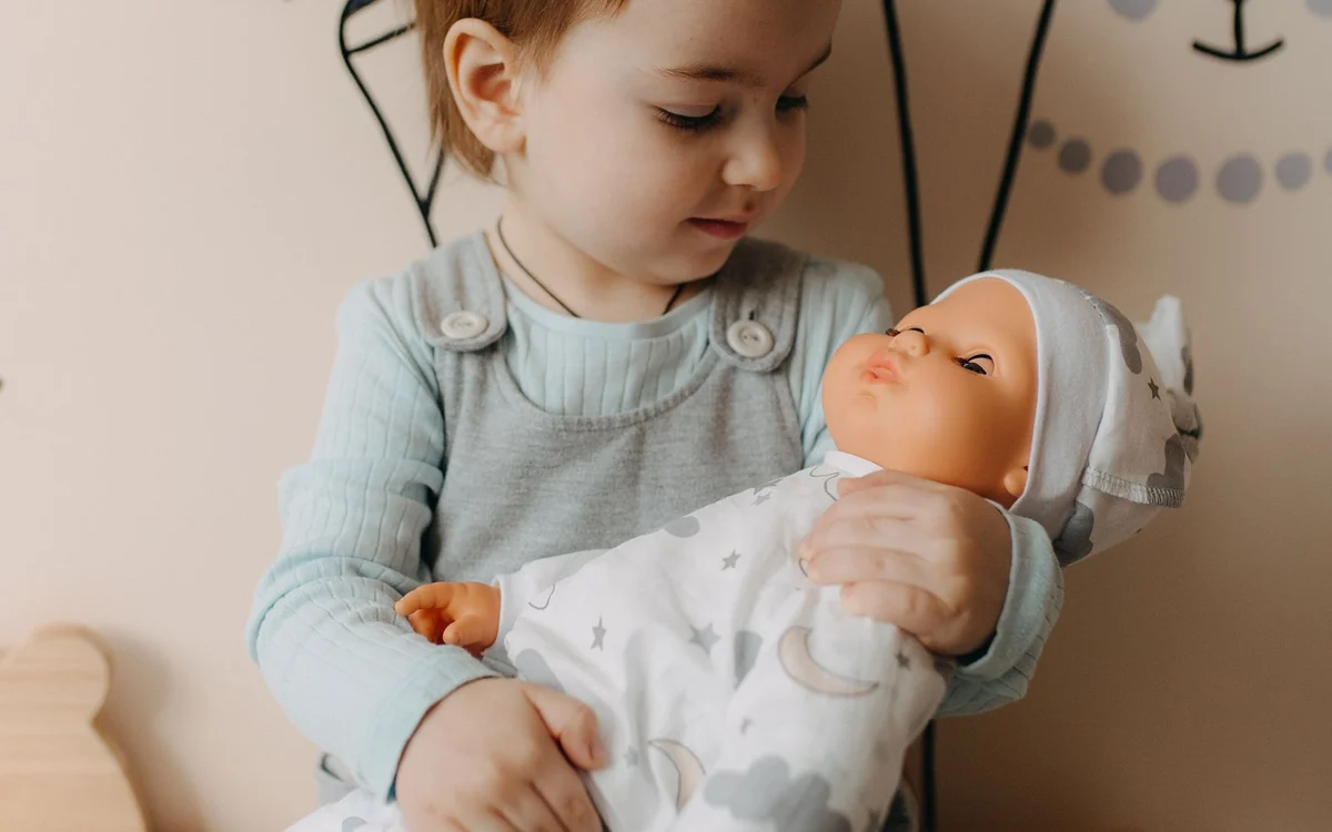 Malutkie dziecko czule trzyma w ramionach lalkę-bobasa