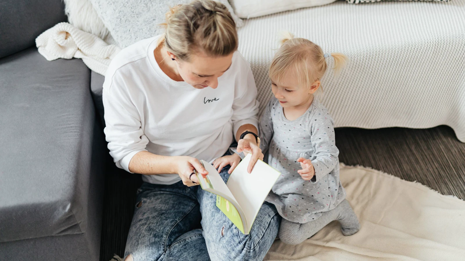 Mama i córeczka razem oglądają książeczkę obrazkową, siedząc na podłodze