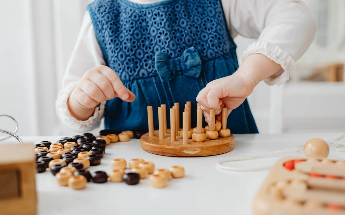 Małe dziecko nakłada drewniane elementy na kołeczki prostej pomocy w duchu Montessori